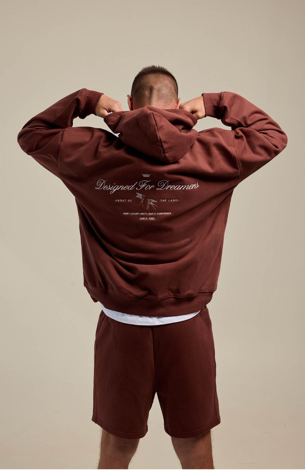 Person wearing a maroon tracksuit with text on the back against a beige background